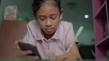 jovencita con auriculares y estudiando desde un teléfono móvil durante la cuarentena en casa. video