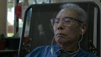 Close-up of a senior man relaxing on a chair while listening to music