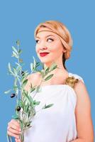 Mujer alegre rubia griega en traje nacional con rama de olivo falsa en sus manos foto