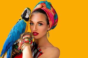 Retrato de mujer joven y atractiva en estilo africano con loro ara en su mano sobre fondo de colores