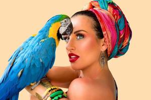 Portrait of young attractive woman in african style with ara parrot on her hand on colorful background photo