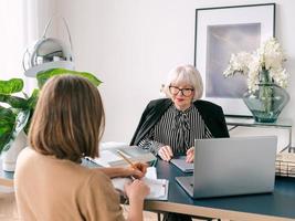 senior stylish woman with young woman discussing work tasks in office. Business, communication, work, ages, collaboration, mentoring concept photo