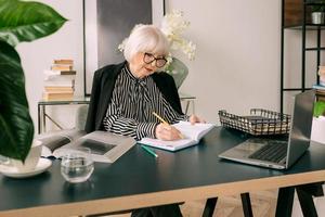 senior beautiful gray hair woman  drinking water during work in office. Work, senior people, water balance, find a solution, experience concept photo