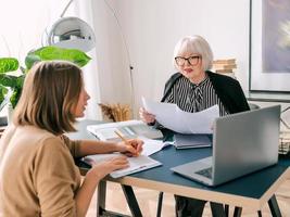 senior stylish woman with young woman discussing work tasks in office. Business, communication, work, ages, collaboration, mentoring concept photo