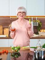 mujer alegre senior con jugo de tomate y apio a dieta en su cocina. crudo, vegetariano, dieta, concepto de cocina foto
