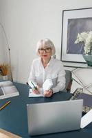 Mujer de cabello gris hermosa senior cansada en blusa blanca leyendo documentos en la oficina. trabajo, personas mayores, problemas, encontrar una solución, concepto de experiencia