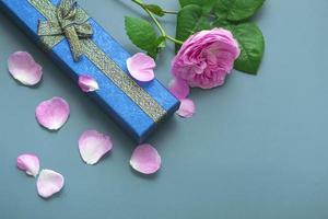 Top view for Father's Day on blue background with rose petals. Close up of gift blue box with gold bows and pink rose. photo