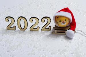 The symbol of the new year is a tiger in a Santa hat on a sleigh in the snow with golden numbers on a background of bokeh lights. New year