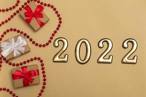 New Year 2022. Top view New Year mockup on beige background red ribbon, gift box, gold numbers and multicolored sparkles. Layout of postcards, invitations.