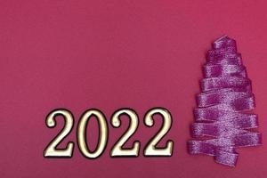 Christmas concept. Purple Christmas tree made from ribbons and gold numbers on a pink background with copy space on top. Template for postcards, packaging. photo