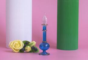 Blue bottle with perfume or oil on a pink background with yellow roses and columns. Cosmetics presentation. Mockup of blue glass perfume or oil bottle for advertising banner photo
