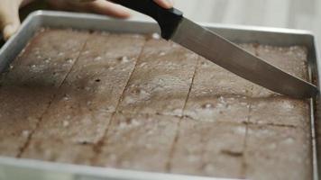 Cutting chocolate brownies cakes on the tray of freshly baked. video