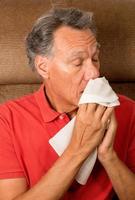 Hombre con gripe estornudando en un pañuelo en su casa foto
