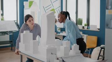 Team of multi ethnic women analyzing maquette on table to design building model video