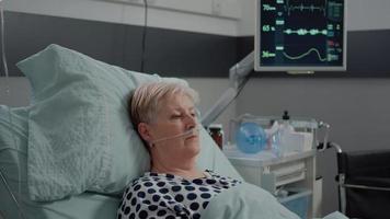 Portrait of elder patient with oxygen tube laying in hospital ward bed