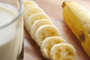 close up of slice of banana glass of milk on table photo