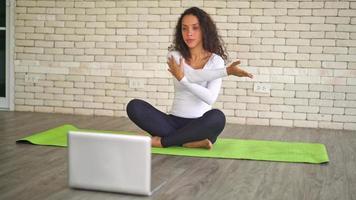 mujer latina influyente enseñando yoga en línea con laptop video