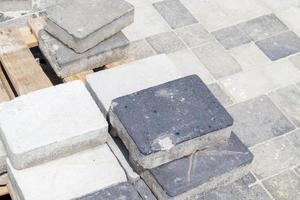 Concrete or paved gray paving slabs or floor or walkway stones stacked on a pallet. Concrete paving slabs in the backyard or road paving. Garden brick path in the courtyard on a sandy foundation. photo