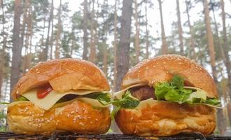 primer plano de dos grandes hamburguesas de bricolaje en el parque en una barbacoa, descansar y cocinar en un picnic en el verano, comida, deliciosos colores brillantes. concepto de comida poco saludable. Comida rápida. foto