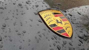 Ukraine, Kiev - March 27, 2020. Porsche logo close up on a black car with raindrops. Hood emblem of a sports car. copy space, editorial photography. German car exhibition on the street. photo