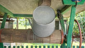 An old water well with a bucket in the garden, a metal handle for lifting water from the ground. Village well under the roof with a rope. Retro well in the countryside. photo