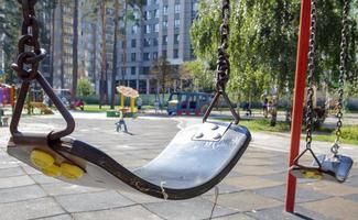 cierre de columpio de bebé vacío en el parque. nuevo columpio de cadena. conjunto de cadenas de columpio negras en un patio de recreo moderno. centrarse en el columpio en el fondo borroso. foto