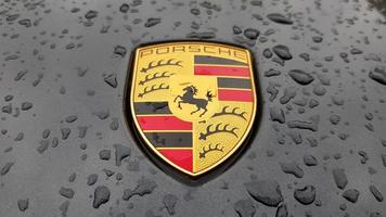 Ukraine, Kiev - March 27, 2020. Porsche logo close up on a black car with raindrops. Hood emblem of a sports car. copy space, editorial photography. German car exhibition on the street. photo