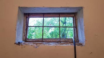 A rectangular basement window is tightened with a metal mesh and a grill. Technical window in the wall of an old gray building. photo