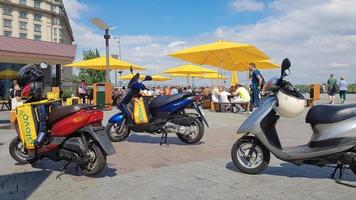 Ukraine, Kiev - August 29, 2020. Lot of parked mopeds with yellow bags with Glovo logo near McDonald's. Courier service that delivers goods ordered through a mobile application. Editorial photography.