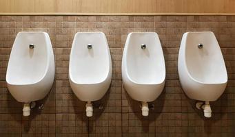 Four urinals lined up on the tiled wall of a modern men's public toilet, no privacy. photo