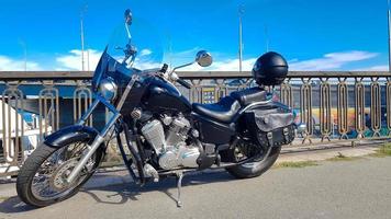 Ucrania, Kiev - 08 de septiembre de 2019. Motocicleta vintage negra estacionada en un puente en el centro de la ciudad rodeado por edificios del centro de la ciudad de entornos urbanos. estilo hipster, sueño de estudiante foto