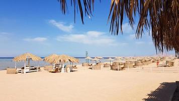 una hermosa playa tropical con sombrillas de paja a orillas del mar rojo en sharm el sheikh. paisaje de verano hermosa playa soleada en egipto. el concepto de vacaciones, viajes, vacaciones. foto