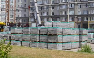 There are many new gray paving slabs on plastic-covered pallets on the construction site. Paving of pedestrian paths on a city street. Foreground. Repair of the sidewalk in the city square. photo