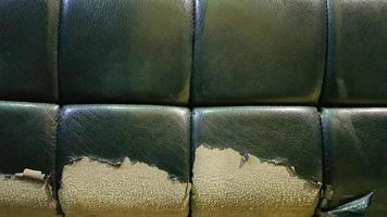 cuero rasgado y maltratado de un sofá verde. Piel de mala calidad, limpieza y restauración de la piel. Detalle de un viejo sillón de cuero vintage. foto