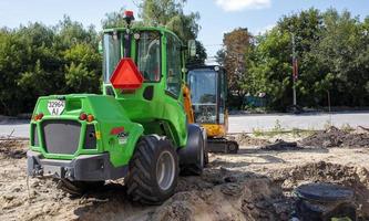 Two small excavators on a large construction site. Bright green on wheels and yellow on tracks. Earthworks and construction. Shovel excavator. Mini loaders. Ukraine, Kiev - August 28, 2021. photo