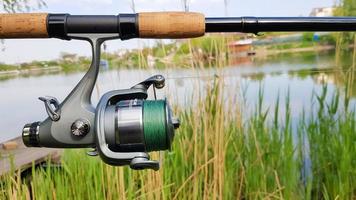 Ukraine, Kiev - June 1, 2020. Fishing reel on a spinning comel close-up on the background of a lake or river. Reel with green fishing line on a natural background. Fisherman's equipment.