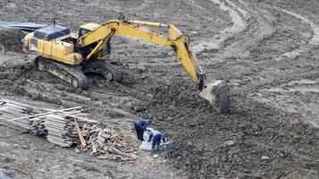 Ukraine, Bukovel - November 20, 2019. Aerial view of a working yellow excavator on a poorly maintained dirt road with people working at a construction site. photo