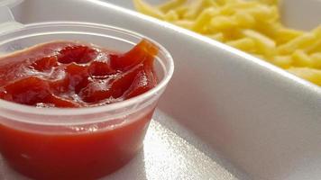 A close-up of golden orange yellow deep fries with tomato ketchup served in a foam container. Fast food takeaway. Unwanted fresh food. photo