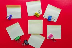 Blank yellow sticky notes and paper clip clips on a red background, business work concept. Yellow commemorative stickers on the red wall. Layout photo