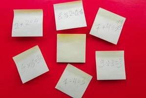 Blank yellow sticky notes with mathematical equations and solving them on a red background, concept of business and study work. Yellow commemorative stickers on the red wall. Layout photo