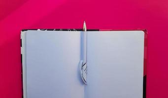 Blank notebook with white pen on a red background. Empty pages of an open book, space for writing and text. View from above. Copy space, flat lay photo