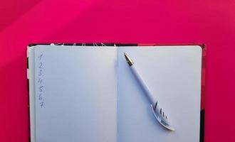 Blank notebook with white pen on a red background. Empty pages of an open book, space for writing and text. View from above. Copy space, flat lay photo