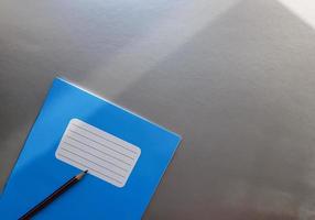 Nuevo cuaderno azul con lápiz sobre una mesa gris con rayos de sol desde el fondo de la ventana foto