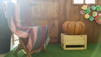 beautiful autumn landscape with one pumpkin and a wooden vintage chair with a plaid on a terrace near a wooden small house. photo