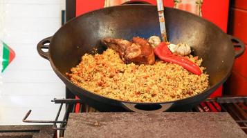 Delicioso pilaf uzbeko en un caldero al aire libre en un festival de comida callejera. cocinar arroz con carne y verduras. una olla grande de cocina nacional kazaja en la calle durante el festival. foto