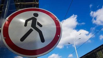 A round road sign of white and red with a black man in the center, prohibiting the movement of pedestrians on a background of blue sky and white clouds. No pedestrians allowed at this place