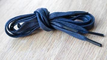 una foto de sujeto de cordones planos azul oscuro con puntas finas para zapatos enrollados y aislados sobre un fondo de madera. accesorio elegante.