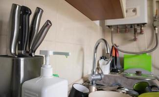 Green sponge and liquid soap dispenser for washing dishes on a dirty sink completely with dishes and kitchen utensils. Washing dishes in the kitchen by hand with detergent and a sponge. photo