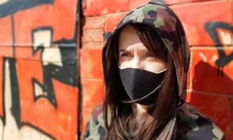 Portrait of a woman in a protective black mask outdoors near an old broken wall. Coronavirus and air pollution concept. A girl wears a protective mask to protect against a pandemic. photo