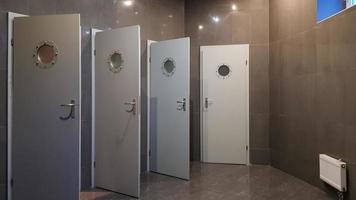 The public building has female and male toilets with four gray doors. Terrier with gray tiles on the walls and floor. photo